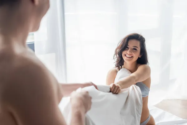 Blurred man pulling blanket with happy and sexy girlfriend — Stock Photo