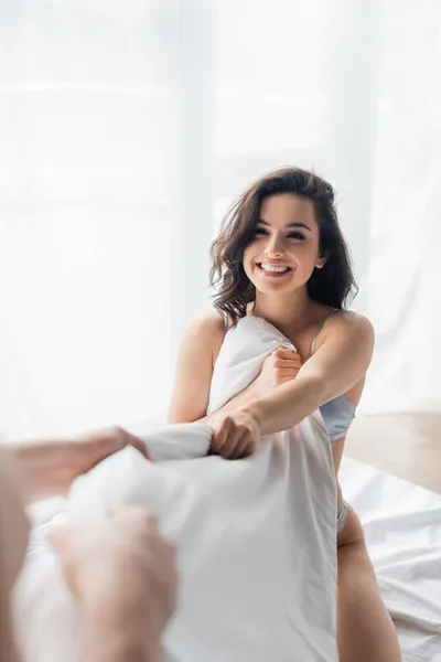 Blurred man pulling blanket with cheerful and sexy girlfriend — Stock Photo