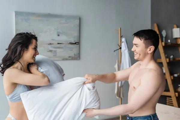 Side view of joyful and sexy couple having pillow fight in bedroom — Stock Photo