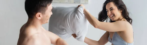 Счастливая и сексуальная пара, дерущаяся подушками в спальне, баннер — стоковое фото