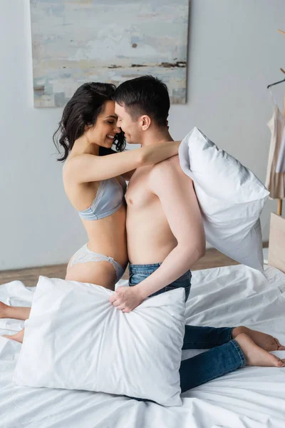 Vue latérale de couple heureux et sexy étreignant tout en tenant des oreillers dans la chambre — Photo de stock