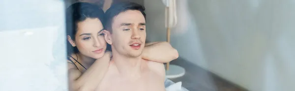 Young woman hugging shirtless man behind window, banner — Stock Photo