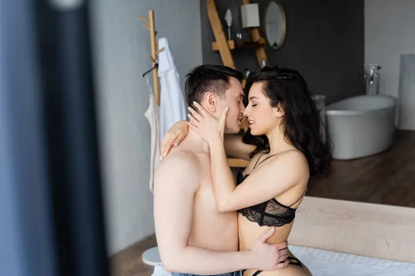Vista lateral de feliz y sexy pareja besándose en casa - foto de stock