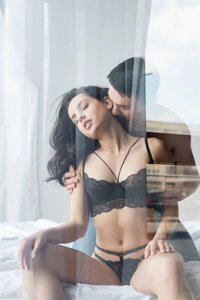 Homem apaixonado beijando mulher sensual em roupa interior de renda atrás de vidro de janela — Fotografia de Stock