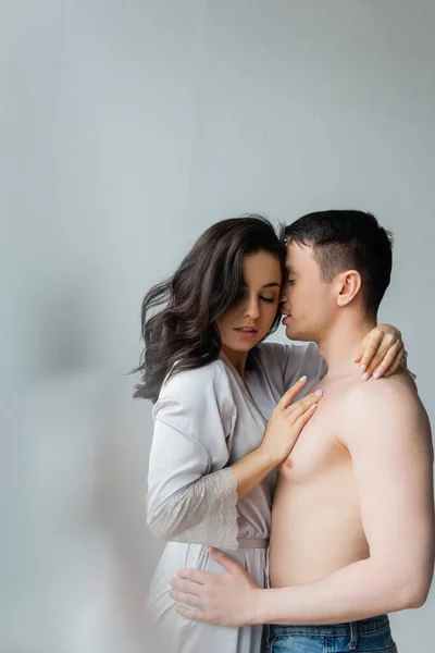 Brunette woman in silk robe hugging shirtless man in bedroom — Stock Photo