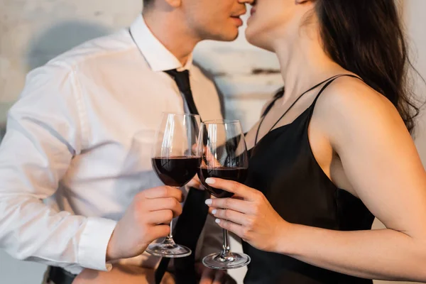 Cropped view of couple holding glasses of red while while kissing at home — Stock Photo