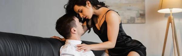 Morena joven en negro deslizamiento vestido seducir novio en el sofá, pancarta — Stock Photo