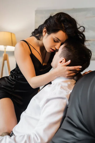 Sexy joven mujer en negro slip vestido seducción novio en sofá - foto de stock