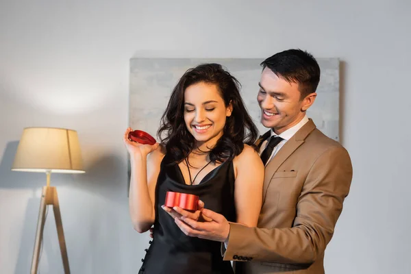 Mujer feliz en vestido de seda sosteniendo presente cerca del hombre en traje - foto de stock