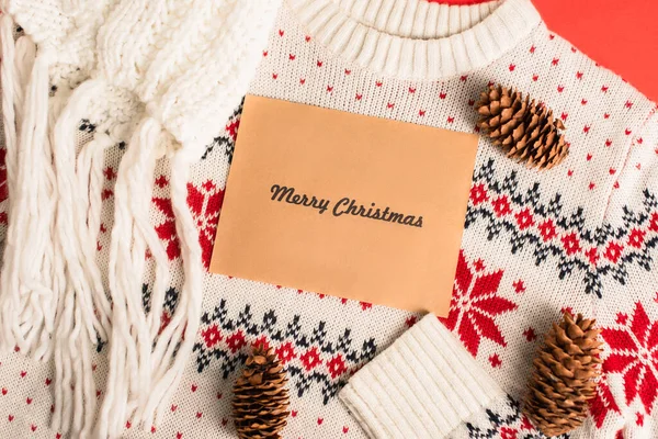 Top view of greeting card with merry christmas lettering near pine cones on knitted sweater — Stock Photo