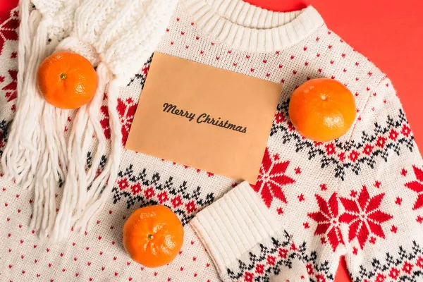 Вид зверху вітальної листівки з веселим різдвяним написом біля мандаринів на в'язаному светрі — стокове фото