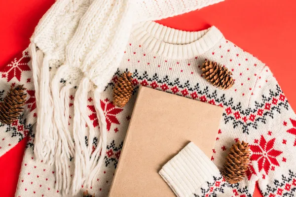 Top view of book near pine cones on knitted sweater and red background — Stock Photo