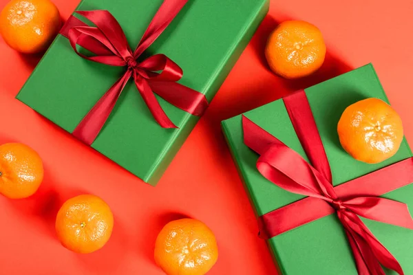 Vue de dessus des cadeaux enveloppés verts près des mandarines mûres sur fond rouge — Photo de stock