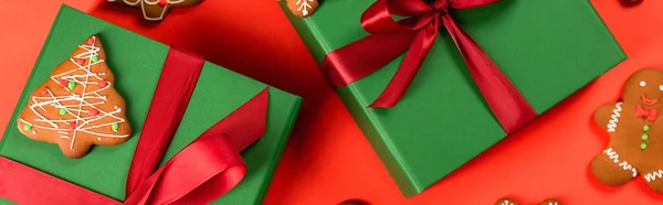 Top view of green wrapped presents near gingerbread cookies on red background, banner — Stock Photo