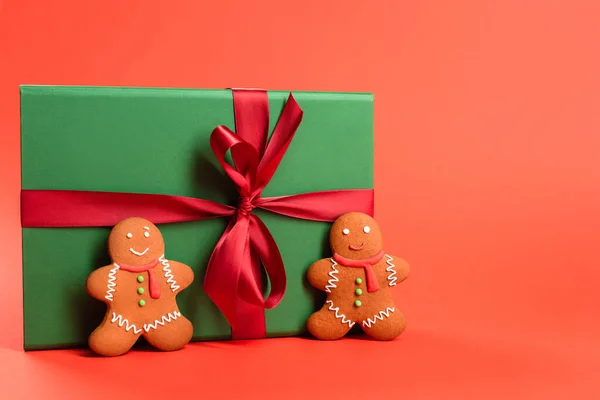 Gingerbread cookies near green wrapped present on red — Stock Photo