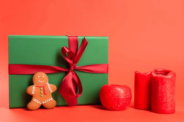 Lebkuchen in der Nähe grün verpacktes Geschenk und Kerzen auf rot — Stockfoto