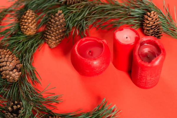 High angle view of pine cones near green branches and candles on red — Stock Photo