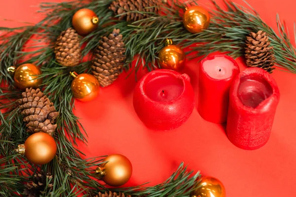 Vista de ángulo alto de conos de pino cerca de ramas verdes con bolas de Navidad y velas en rojo - foto de stock