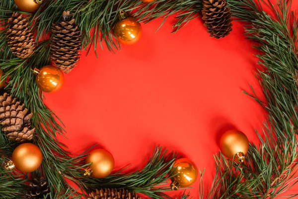 Top view of pine cones near green branches with christmas balls on red — Stock Photo