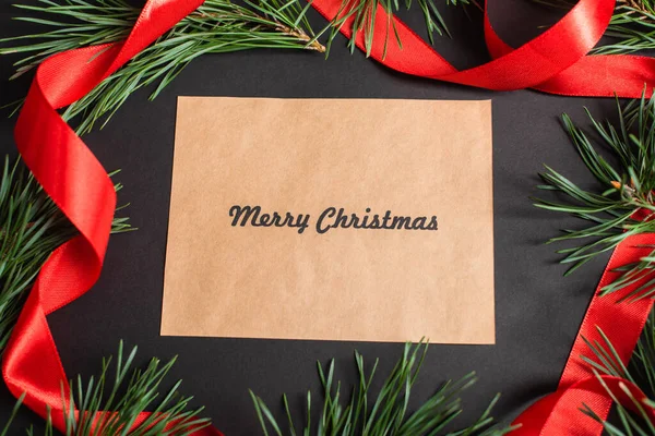 Vue du haut de la carte de vœux avec joyeux lettrage de Noël près des branches de sapin et ruban rouge sur noir — Photo de stock