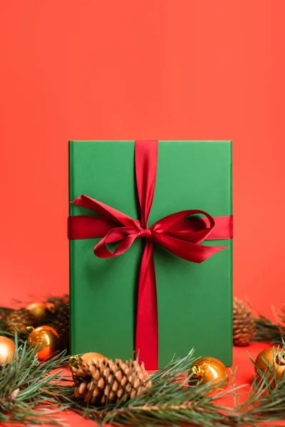 Wrapped present near pine cones and green branches with christmas balls on red — Stock Photo