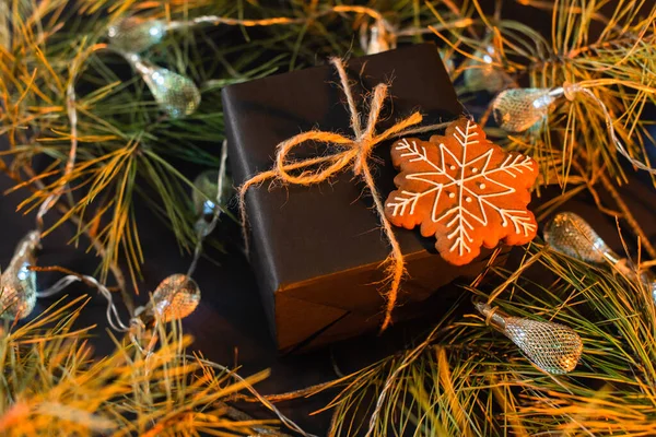 Vue grand angle du noir enveloppé présent avec biscuit au pain d'épice près des branches vertes avec guirlande — Photo de stock