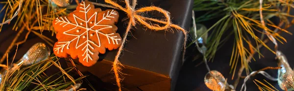 High angle view of wrapped black present with gingerbread cookie near green branches with garland, banner — Stock Photo