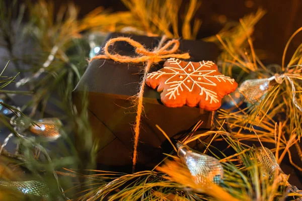 Présent noir enveloppé avec biscuit au pain d'épice près des branches vertes avec guirlande — Photo de stock