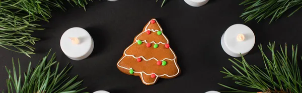 Vue du dessus du biscuit au pain d'épice près des bougies et des branches de pin sur noir, bannière — Photo de stock