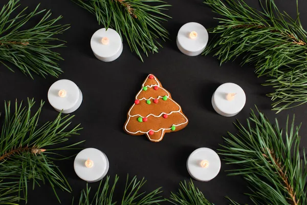 Top view of gingerbread cookie near candles and pine branches on black — Stock Photo
