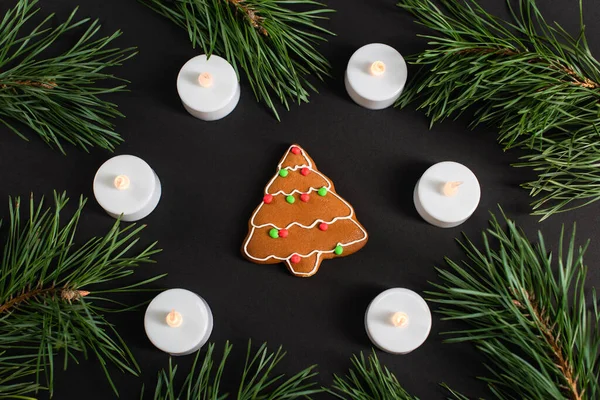 Top view of gingerbread cookie near candles and pine branches on black — Stock Photo