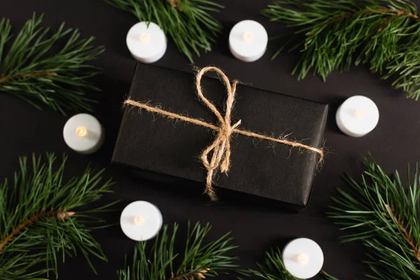 Vista dall'alto della confezione regalo vicino a candele e rami di pino su nero — Foto stock