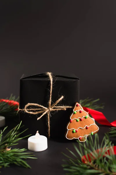 Presente embrulhado perto de ramos de abeto, biscoito de gengibre e vela em preto — Fotografia de Stock