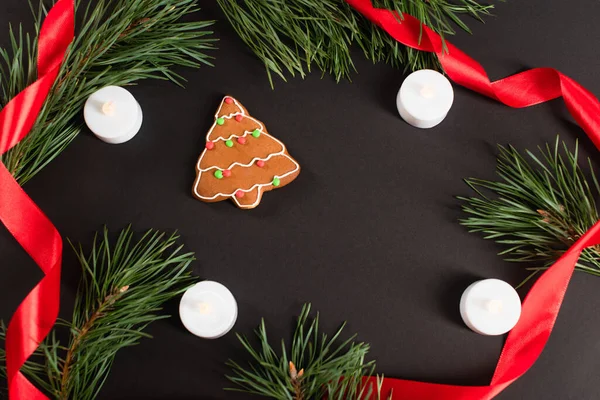 Top view of gingerbread cookie near candles, fir branches and red ribbon on black — Stock Photo