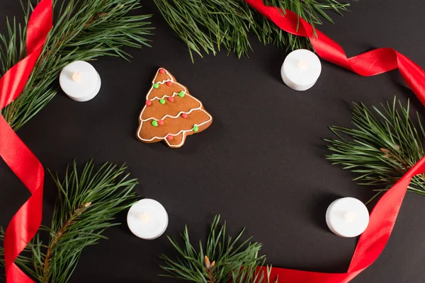 Blick von oben auf Lebkuchen in der Nähe von Kerzen, Tannenzweigen und roter Schleife auf schwarz — Stockfoto