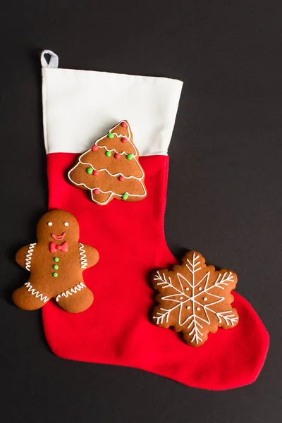 Top view of different shapes gingerbread cookies on red christmas stocking isolated on black — Stock Photo