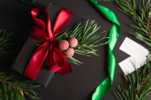 Top view of wrapped gift box with decoration near green ribbon on black — Stock Photo