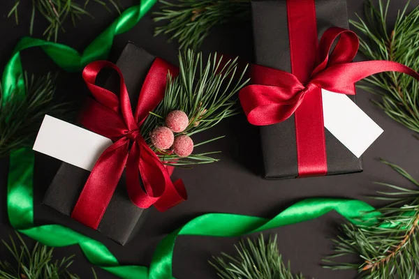 Top view of wrapped gift boxes with blank cards near blurred fir branches on black — Stock Photo