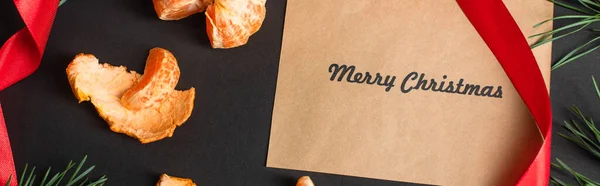 Верхний вид ремесленной бумаги с веселыми рождественскими буквами рядом с очищенными мандаринами на черном, баннер — стоковое фото