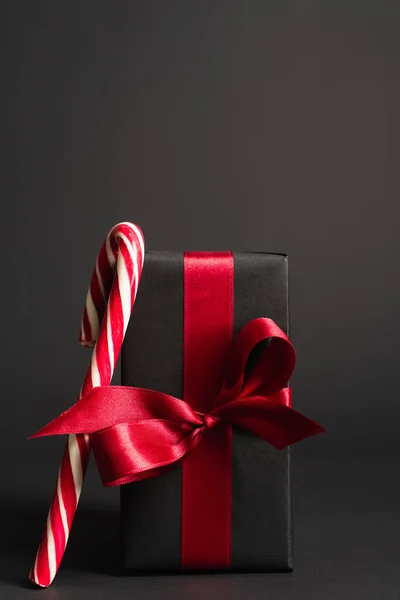 Смугаста цукеркова тростина біля загорнутого подарунка з червоною стрічкою на чорному — стокове фото