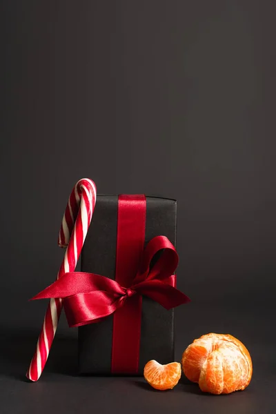 Canne à bonbons rayée près présent enveloppé avec ruban rouge et mandarine sur noir — Photo de stock