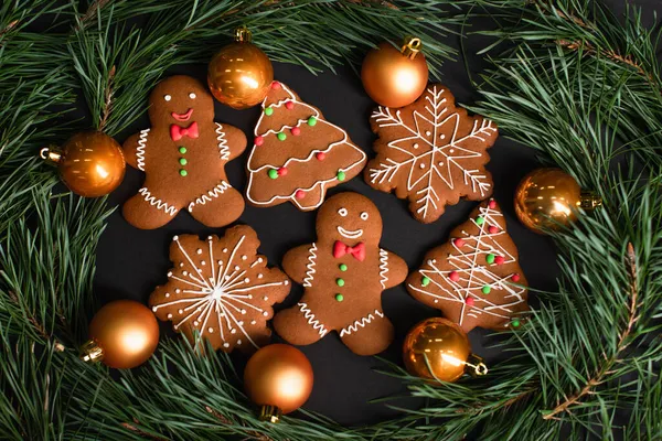 Vista dall'alto di biscotti di pan di zenzero vicino a palle di Natale d'oro vicino a rami di abete su nero — Foto stock