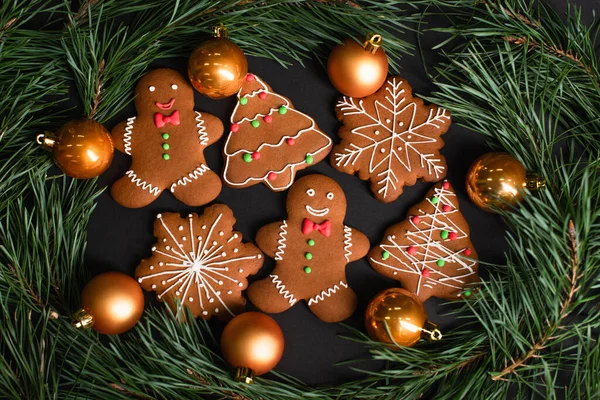 Vista superior de galletas de jengibre cerca de bolas de Navidad de oro cerca de ramas de abeto en negro - foto de stock