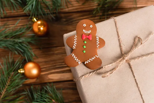 Top view of gingerbread cookie on gift box near blurred pine branches on wooden surface — Stock Photo