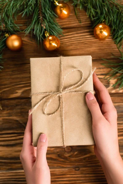 Vue recadrée de la femme tenant la boîte cadeau enveloppée près des boules de Noël et des branches sur la surface en bois — Photo de stock