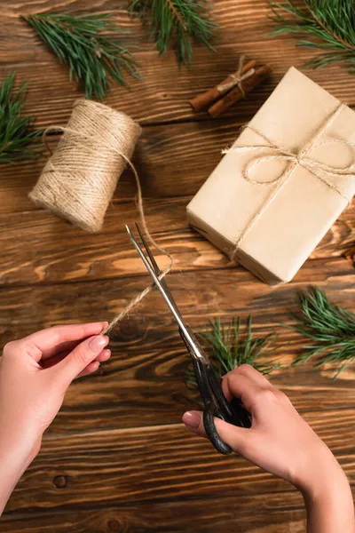 Cropped view of woman holding scissors while cutting string near present on wooden surface — Stock Photo