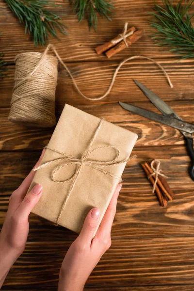 Vue recadrée de la femme tenant la boîte cadeau enveloppée près des ciseaux sur la surface en bois — Photo de stock