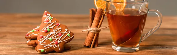 Taza de té de vidrio con rodajas de naranja cerca de palitos de canela y galletas de jengibre aisladas en gris, pancarta - foto de stock