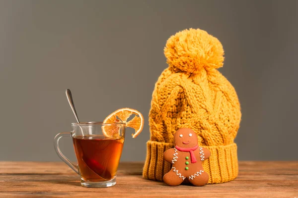 Glass cup of tea with sliced orange near knitted hat and gingerbread cookie isolated on grey — Stock Photo