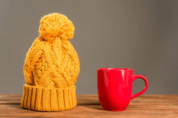 Tazza di tè rosso vicino a cappello lavorato a maglia su superficie di legno isolata su grigio — Foto stock